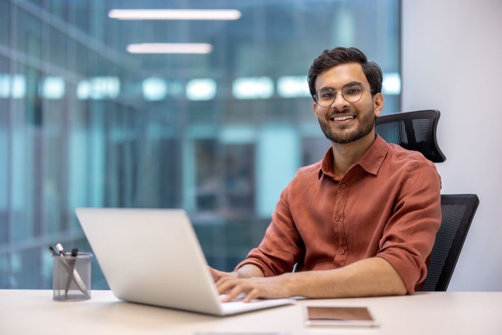 A young professional working on a laptop in a modern office, embodying productivity and job satisfaction in a Business Setup